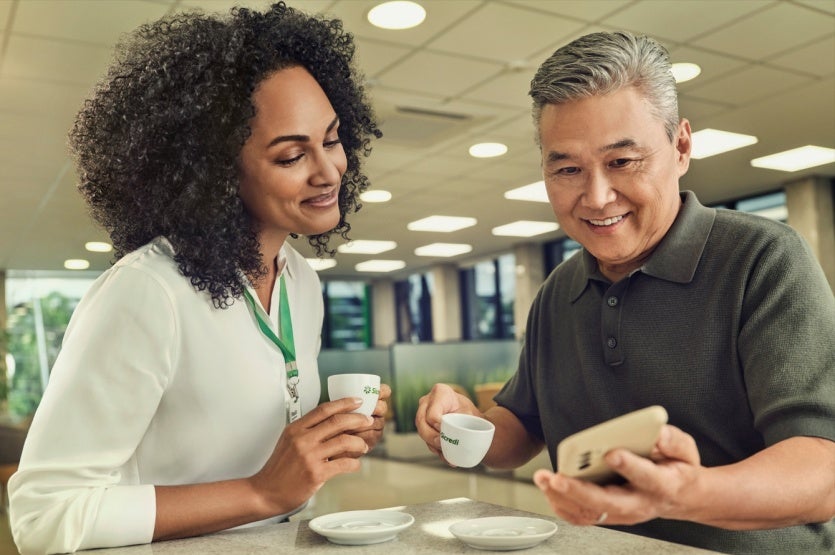 duas pessoas olhando o celular, tomando café e conversando