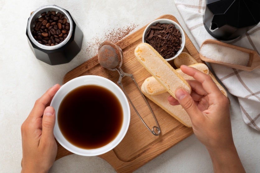 Café em uma mesa com uma pessoa segurando um biscoito.