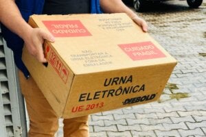 Caixa com urna eletrônica sendo carregada por funcionário da Justiça Eleitoral.