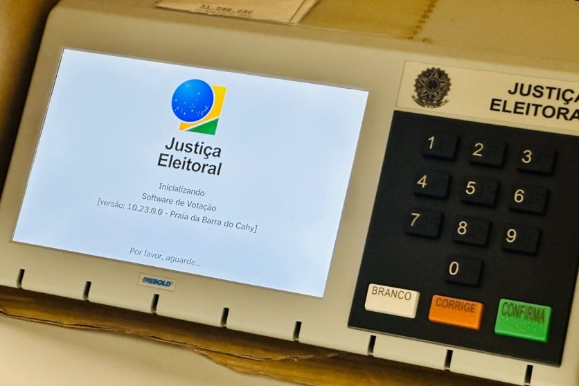 Urna eletrônica com a tela da Justiça Eleitoral no dispositivo.