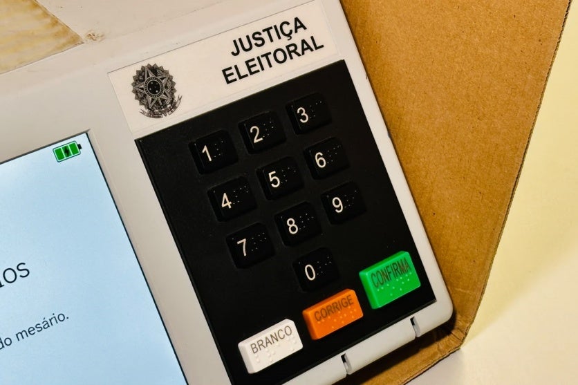 Foto lateral da urna eletrônica na cabine de votação.
