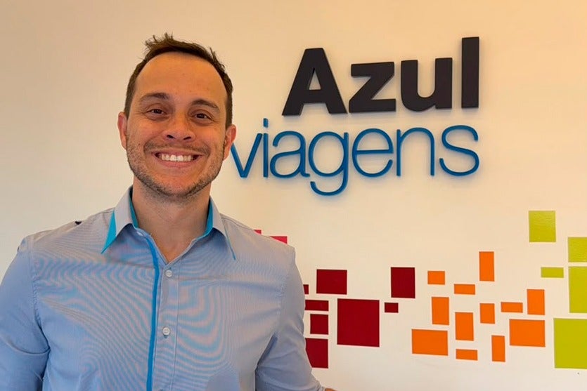 Representante da Azul Viagens posando com o logo da empresa ao fundo.