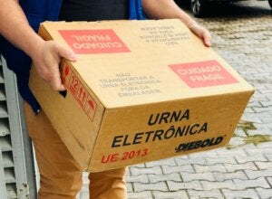 Funcionário do TRE carregando caixa com urna eletrônica.